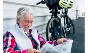 older man sitting next to his bicycle reading newspaper